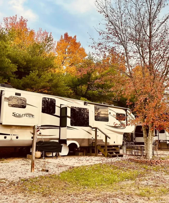 A large Grand Design Solitude fifth-wheel RV setup at a spacious, gravel campsite surrounded by autumn foliage at Kountry Resort Campground.