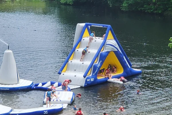 Children and families climbing and sliding down the massive blue and yellow Summit Express inflatable water slide at the Kountry Resort Campground lake.