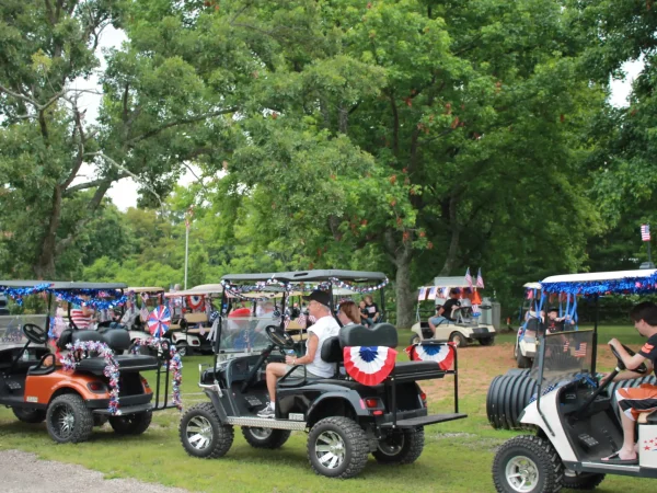 A lineup of custom golf carts decorated with patriotic red, white, and blue tinsel and banners, preparing for the holiday parade at Kountry Resort Campground.
