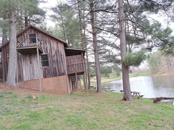 A multi-story rustic wooden cabin featuring upper and lower balconies, built on a grassy hill overlooking the private resort lake at Kountry Resort Campground.