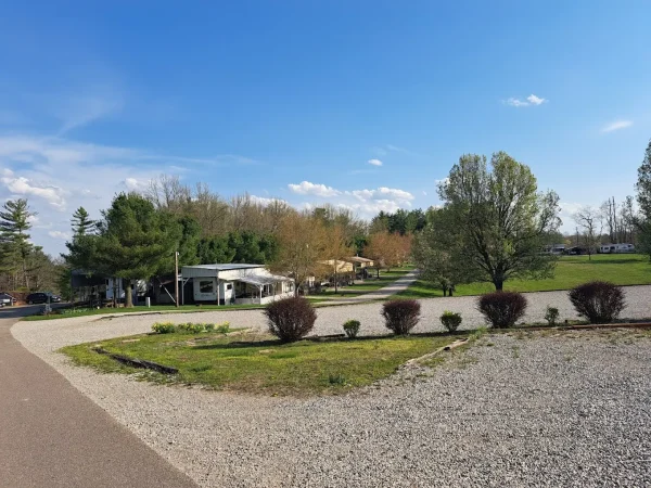 A wide view of gravel RV camping sites, paved access roads, and permanent park models surrounded by green lawns and mature trees at Kountry Resort Campground.