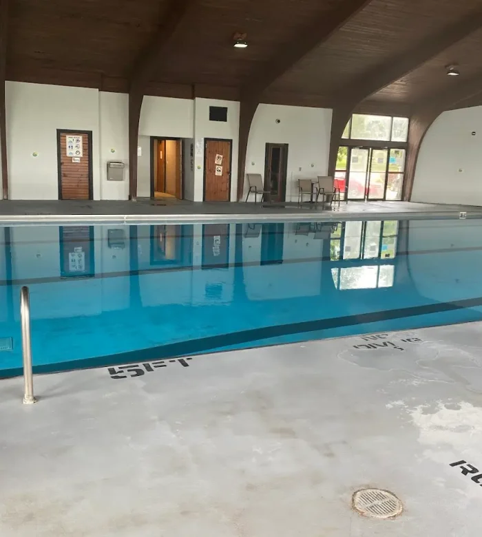 A wide view of the indoor swimming pool deck showing the pool ladders, depth markers, and changing room entryways under a vaulted wood ceiling at Kountry Resort Campground.