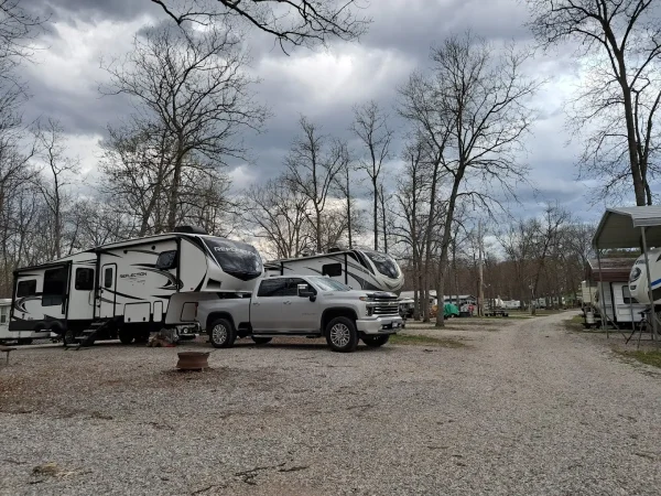 A silver Chevrolet pickup truck parked next to a modern Grand Design Reflection fifth-wheel travel trailer at a gravel campsite at Kountry Resort Campground.
