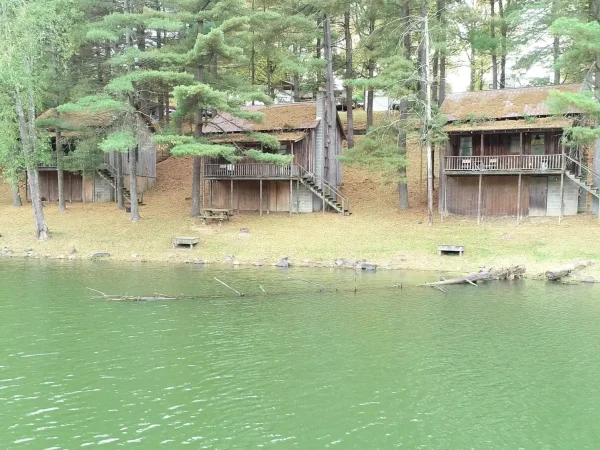 A wide view of a sandy beach area with lawn chairs and picnic tables along the edge of a calm lake, with an inflatable water park visible in the background at Kountry Resort Campground.
